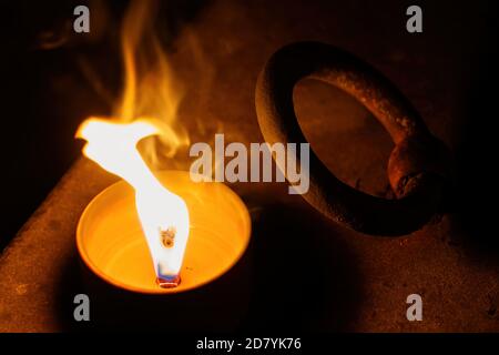 Candela che brucia luminosa di notte su una vecchia lastra di pietra tomba con manico in metallo arrugginito. Foto Stock