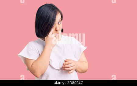 Donna bruna con sindrome di Down indossare casual tshirt bianca che punta all'occhio che ti guarda gesto, espressione sospetta Foto Stock