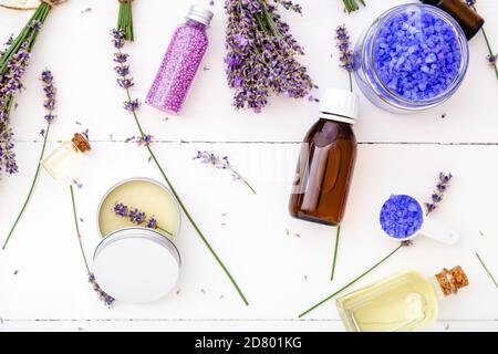 Prodotti da bagno e fiori di lavanda. Sapone sale marino olio essenziale, burro per il corpo, olio per massaggi, liquido. Piatto in legno bianco Foto Stock