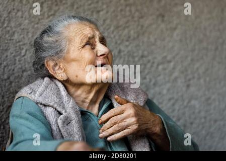 Donna anziana. Ritratto di una donna molto vecchia e stanca di vita rugosa all'aperto vicino al muro della sua casa. Immagine con spazio di copia Foto Stock