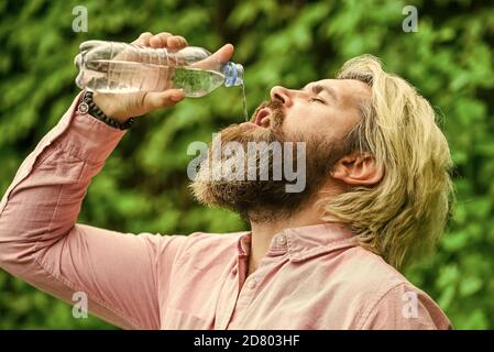 Equilibrio dell'acqua. Uomo sopportato turista acqua potabile bottiglia di plastica natura sfondo. Calore estivo. Acqua potabile. Ragazzo assetato che beve acqua in bottiglia. Stile di vita sano. Sicurezza e salute. Foto Stock