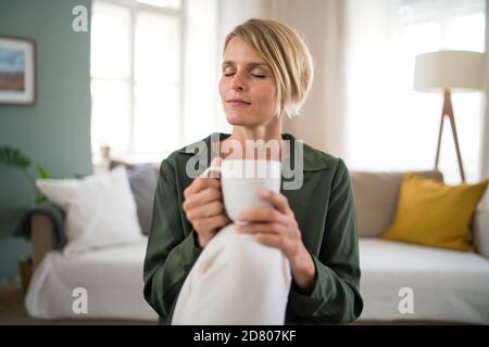 Ritratto di donna che medita all'interno in ufficio, tenendo una tazza di tè. Foto Stock