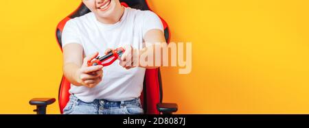 Donna seduta dietro la sedia da gioco nelle mani che tiene in rosso gamepad su sfondo giallo Foto Stock