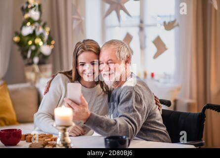 Giovane donna con nonno in casa a Natale, prendendo selfie. Foto Stock