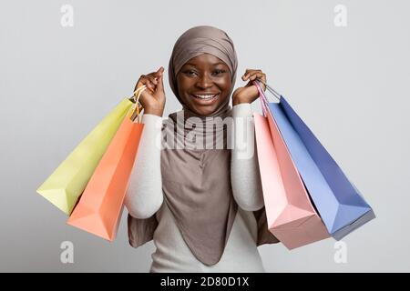 Vendite stagionali. Donna nera eccitata in hijab che tiene i lotti delle borse della spesa Foto Stock