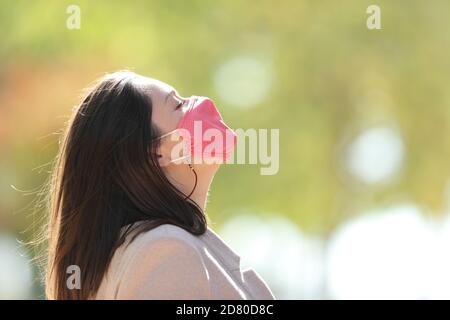 Ritratto con vista laterale di un imprenditore rilassato con la maschera che respira aria fresca in un parco Foto Stock