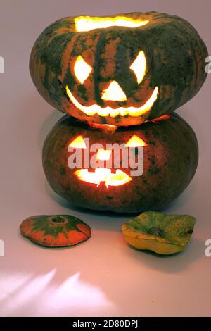 halloween grande zucca a righe su zucca più piccola. le cime tagliate si trovano sotto di loro. spaventoso bagliore rosso viene dall'interno Foto Stock