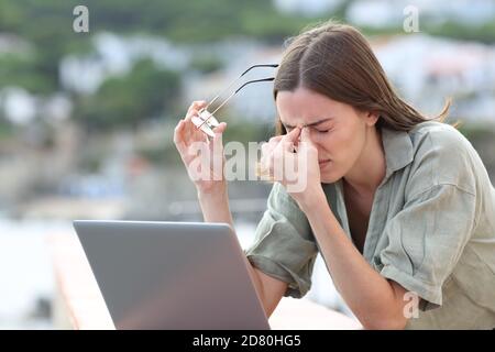 Donna stressata che usa il laptop che soffre di eyestrain lamentandosi all'aperto in un balcone Foto Stock