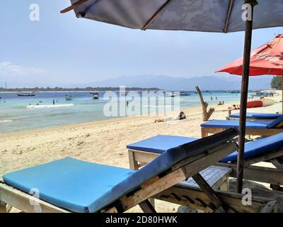 Vista verso est attraverso le acque blu limpide verso Gili Meno e Lombok con sdraio sulla spiaggia a Gili Trawangan, Indonesia Foto Stock