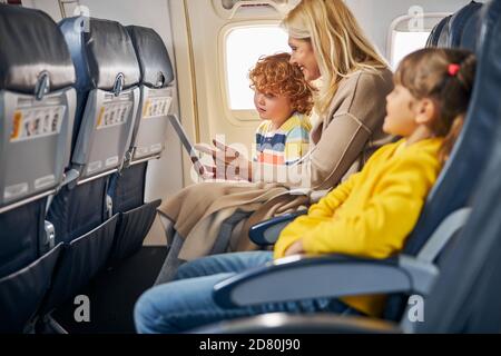 Donna all'interno di un aereo che mostra una tavoletta ad un ragazzo Foto Stock
