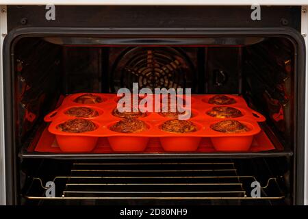 Involtini di cannella fatti in casa da impasto di lievito cotto in uno stampo di silicone rosso all'interno di un forno domestico. Messa a fuoco superficiale. Foto Stock