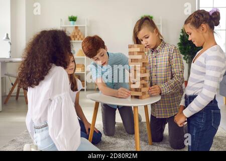 Gruppo di amici gioca una partita di jenga. Ragazzo sta per raccogliere una figurina di legno dalle torri. Foto Stock