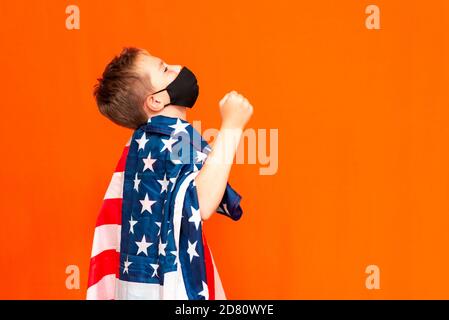 Vista laterale calma ragazzo indossando maschera nera come un boxer sulla spalla bandiera usa su sfondo arancione Foto Stock