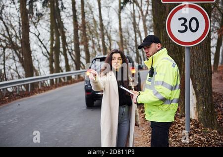 Ufficiale di polizia maschile in uniforme verde che parla con la proprietaria femminile della vettura su strada Foto Stock