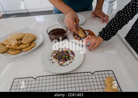 padre e figlia che decorano i biscotti vicino alle mani Foto Stock