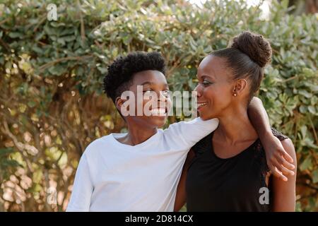 Sorridente ragazzo nero presteen con braccio intorno spalla di felice mamma Foto Stock