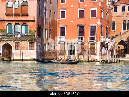 Il gondoliere prende i turisti sulla sua gondola sul Canal Grande passando davanti a edifici storici. I turisti tornano a Venezia, ma molto meno che negli ultimi anni. Foto Stock