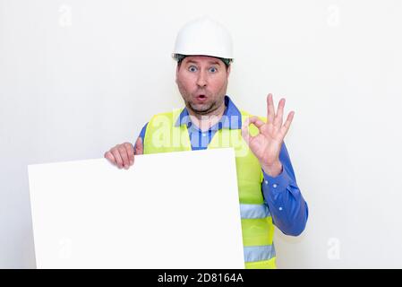 Primo piano uomo ingegnere che indossa un casco e un gilet riflettore, in piedi e tenendo un cartellone. Sfondo bianco. Foto Stock