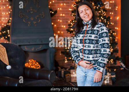 Donna felice in abiti di natale in piedi nel nuovo anno camera decorata Foto Stock