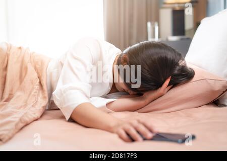 donna assonnata spegnere la sveglia sullo smartphone mentre si addormenta letto Foto Stock