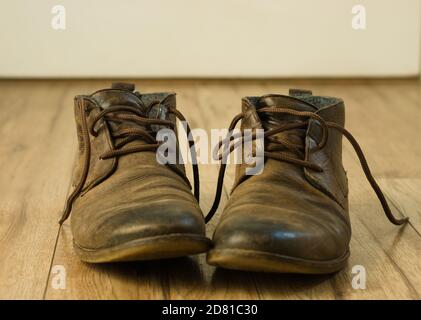 Vecchi stivali marroni usurati su un pavimento di legno Foto Stock