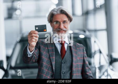 Uomo con capelli grigi e baffi in piedi contro l'auto moderna interni con carta di credito in mano Foto Stock