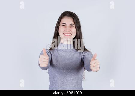 Ritratto di una allegra studentessa che mostra i pollici in su. Ragazza felice in abiti casual guardando la macchina fotografica con gioioso e affascinante sorriso. Spazio di copia, WI Foto Stock