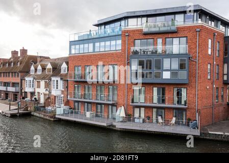 Moderno edificio di appartamenti accanto a tradizionali case a schiera britanniche lungo un fiume in una nuvolosa giornata di primavera Foto Stock