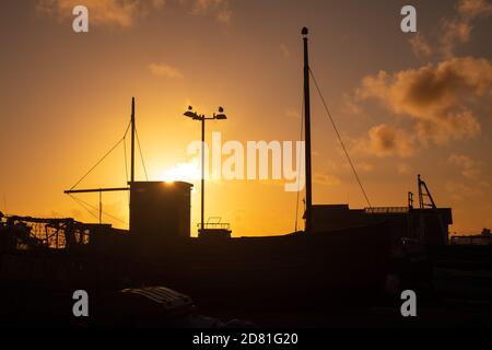 La silhouette di una barca da pesca contro un tramonto d'autunno a Rock'A'nore, nel centro storico di Hastings, Sussex Foto Stock