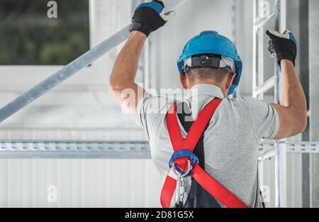 Lavoratori edili che indossano imbracature di sicurezza arrampicate su ponteggi in alluminio nella zona di costruzione. Foto Stock