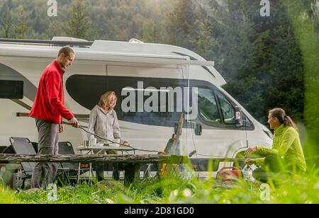Tre amici caucasici nel loro 40 Hanging out su un campeggio con Camper Van Classe B veicolo ricreativo. Parcheggio per camper con caminetto. Esterno e R Foto Stock