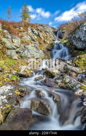 Bella foto ad angolo basso di cascata nelle montagne di Altai in Siberia, Russia. Laghi di Karakolskie. Acqua e nuvole lisce e setose. Cielo blu con nuvole a Foto Stock