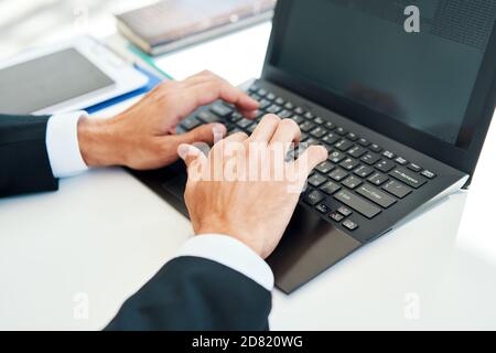 Primo piano le mani dell'uomo che scrivano su un computer portatile. Uomo d'affari che lavora in ufficio Foto Stock