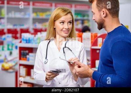 farmacista professionale femmina aiutare il cliente maschile scelta farmaci da prescrizione, consultare i clienti malati. shopping in farmacia, prendendo consiglio da giovane chimico. Consumismo, personale cordiale Foto Stock