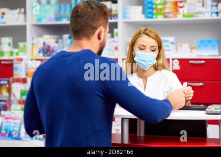 giovane professionista dract dare farmaci al cliente in farmacia moderna, consultare e raccomandare, indossare maschera medica di protezione dal coronavirus covid-19 Foto Stock