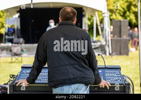 Vista posteriore di un giovane uomo che indossa una giacca in piedi dietro l'elettronica equalizzatore audio mentre si sta fissando al palco arrangiamento nella fiesta culturale Foto Stock