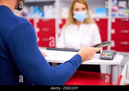 i clienti tagliati pagano per i farmaci in farmacia, concentrarsi in mano con smartphone e terminale per il pagamento Foto Stock