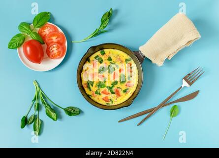 Su una piccola padella di ghisa, omelette con spinaci freschi, pomodori, spezie ed erbe italiane. Orientamento orizzontale, fuoco selettivo. Foto Stock