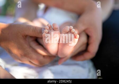 I piedi del neonato nelle mani della madre e del padre. All'aperto. Primo piano Foto Stock