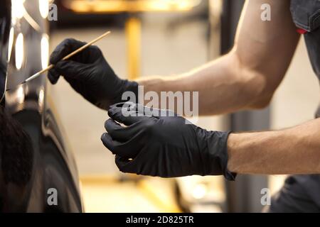 uomo meccanico sicuro auto usando spazzola per verniciare un'automobile, applicando vernice di automobile rappresentativa nera dopo la graffiatura Foto Stock