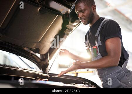 riparando in action. dipendente del tipo hardworking in uniforme lavora nel salone dell'automobile, meccanico sicuro dell'automobile è lavoratore professionale di servizio Foto Stock