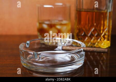 Sigaro illuminato in un posacenere rotondo in vetro da primo piano, messa a fuoco selettiva, bokeh. Foto Stock