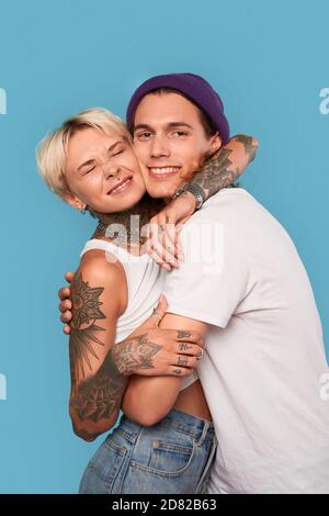 Stile libero. Giovane coppia tatuata in piedi isolato su hugging blu sorridente felice primo piano Foto Stock