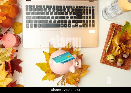 Ciao settembre. piatto con taccuino, foglie, castagne, banca piggy, carta di credito e laptop su tavola bianca. Foto Stock