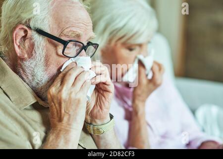 Primo piano di uomo anziano e donna con un naso che cola usando tovaglioli di carta. Concetto di cura e salute Foto Stock