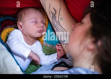 Ritratto del bambino neonato che dorme tranquillamente su uncinetto lavorato a maglia letto con madre che riposa oltre al bambino con coperta Foto Stock