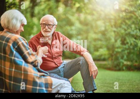 Uomo anziano felice che guarda la moglie mentre tiene i bicchieri con il vino rosso all'aperto. Relazione e concetto di famiglia. Spazio di copia Foto Stock