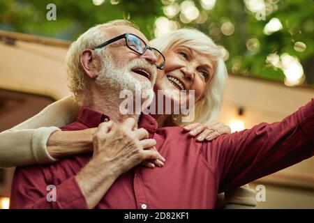 Sorridendo uomo e donna senior facendo selfie e abbracciando mentre si sta in piedi vicino al loro camper. Concetto di stile di vita Foto Stock