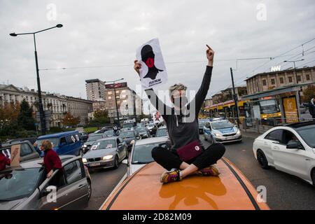 Un protestante che indossa una maschera si siede sul tetto di un'auto e tiene il manifesto dello sciopero delle donne durante la protesta.migliaia di persone sono scese per le strade della Polonia per un quinto giorno di proteste contro una sentenza della corte costituzionale che avrebbe imposto un divieto quasi totale di aborto in Polonia. Hanno occupato diverse rotatorie chiave nel centro della città per bloccare il traffico e ha cantato slogan anti-governo, brandiando il simbolo di protesta - un fulmine rosso. La Women's Strike Organisation (Strajk Kobiet), che ha avviato le proteste in Polonia, ha scelto come motto: Questa è la guerra! (Per gioire wojna!) e. Foto Stock