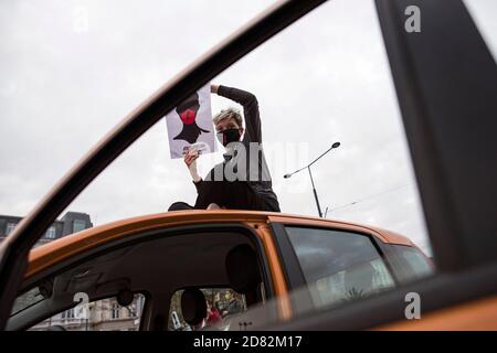 Un protestante che indossa una maschera si siede sul tetto di un'auto e tiene il manifesto dello sciopero delle donne durante la protesta.migliaia di persone sono scese per le strade della Polonia per un quinto giorno di proteste contro una sentenza della corte costituzionale che avrebbe imposto un divieto quasi totale di aborto in Polonia. Hanno occupato diverse rotatorie chiave nel centro della città per bloccare il traffico e ha cantato slogan anti-governo, brandiando il simbolo di protesta - un fulmine rosso. La Women's Strike Organisation (Strajk Kobiet), che ha avviato le proteste in Polonia, ha scelto come motto: Questa è la guerra! (Per gioire wojna!) e. Foto Stock